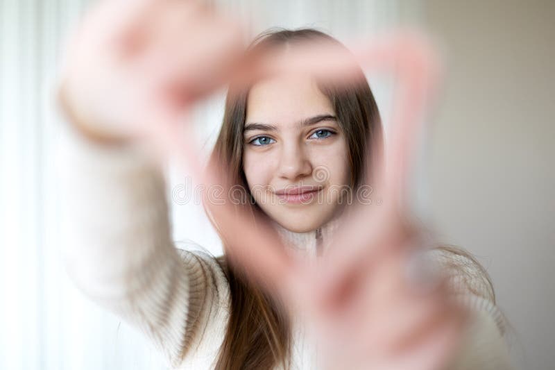 Fille encadrant son visage avec ses mains en forme de coeur. Une jeune fille aux cheveux bruns sourit doucement tout en encadrant photos libres de droits