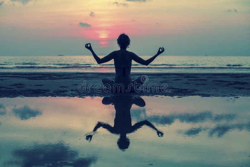 Fille faisant la méditation dans la plage d'océan Avec la réflexion dans l'eau photographie stock