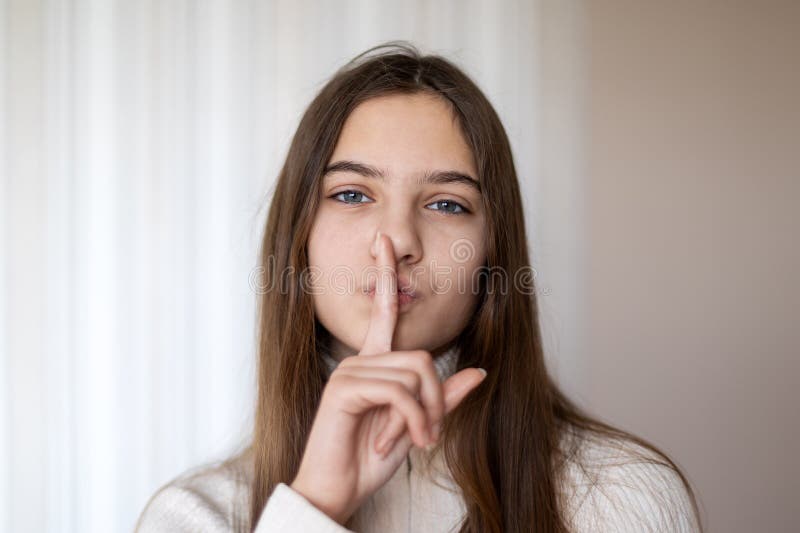 Fille faisant un geste tranquille avec son doigt sur ses lèvres. Une jeune fille aux cheveux bruns droits gestes pour le silence p photos stock