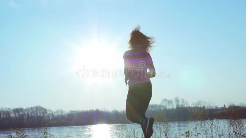 Fille folâtre pulsant le long de la berge pendant le lever de soleil ou le coucher du soleil Le concept sain de mode de vie de la