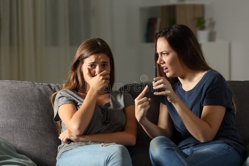 Girl scolding her sad friend about media content sitting on a couch in the living room at home. Girl scolding her sad friend about media content sitting on a couch in the living room at home