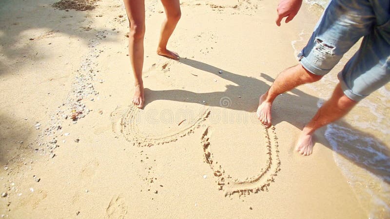 Fille Guy Feet Barefoot Draw Heart sur la plage de sable au bord de vague