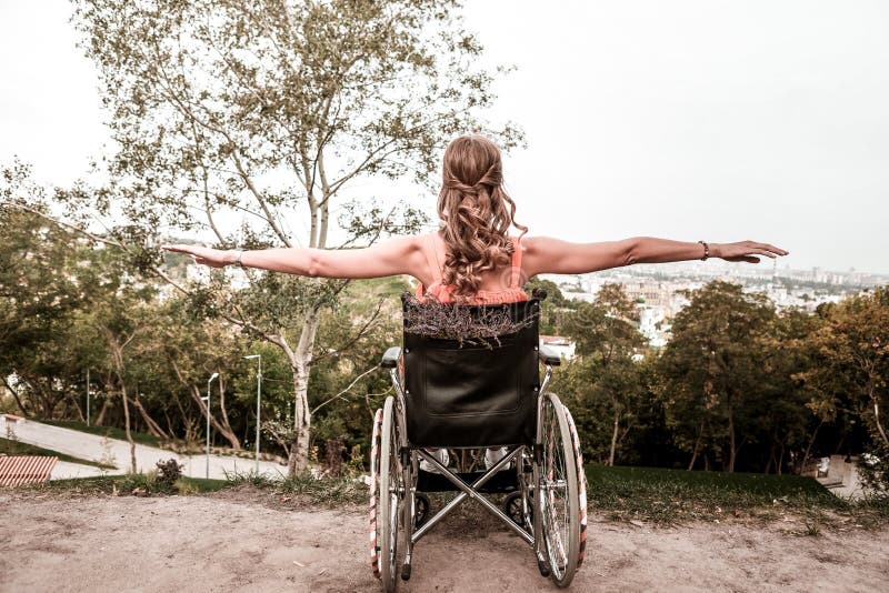 Fille handicapée s'asseyant dans le fauteuil roulant et faisant des exercices. Peu d'exercice Fille handicapée sûre calme s'asseyant dans le fauteuil roulant et mettant des mains tout en faisant s'exerce en parc