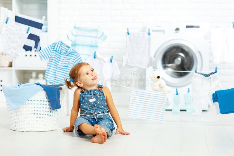 Fille heureuse d'amusement d'enfant petite pour laver des vêtements et des rires dans le laund images stock Fille heureuse d'amusement d'enfant petite pour laver des vêtements et des rires dans le laund images stock