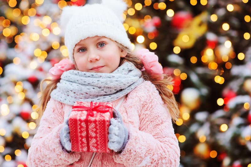 Fille heureuse d'enfant jugeant le cadeau de Noël extérieur sur la promenade dans la ville neigeuse d'hiver décorée pendant des v photos stock Fille heureuse d'enfant jugeant le cadeau de Noël extérieur sur la promenade dans la ville neigeuse d'hiver décorée pendant des v photos stock