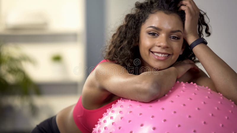 Fille heureuse de sport souriant à la caméra, se reposant sur la boule de forme physique après séance d'entraînement de gymnase photographie stock Fille heureuse de sport souriant à la caméra, se reposant sur la boule de forme physique après séance d'entraînement de gymnase photographie stock