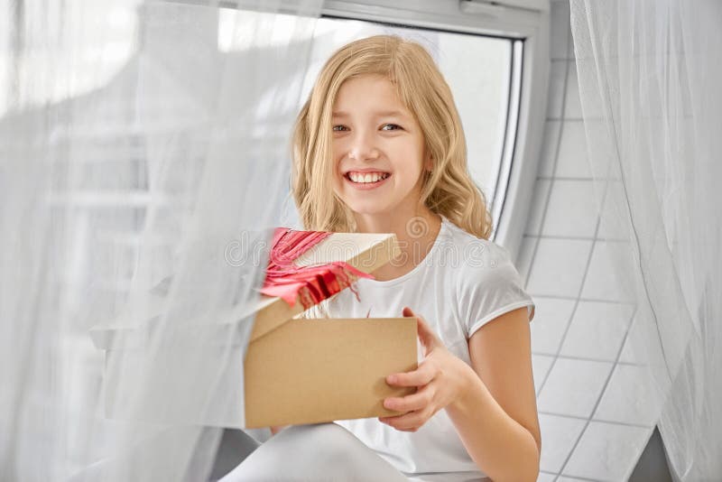 Fille heureuse s'asseyant près de la fenêtre, tenant le présent image libre de droits Fille heureuse s'asseyant près de la fenêtre, tenant le présent image libre de droits