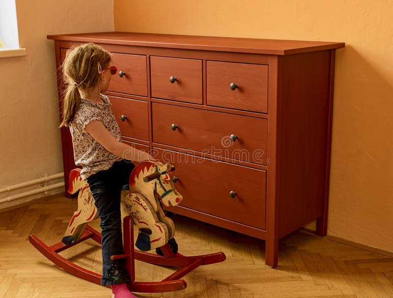 Fille heureuse sur le cheval d'oscillation La petite fille porte les lunettes rouges photographie stock Fille heureuse sur le cheval d'oscillation La petite fille porte les lunettes rouges photographie stock