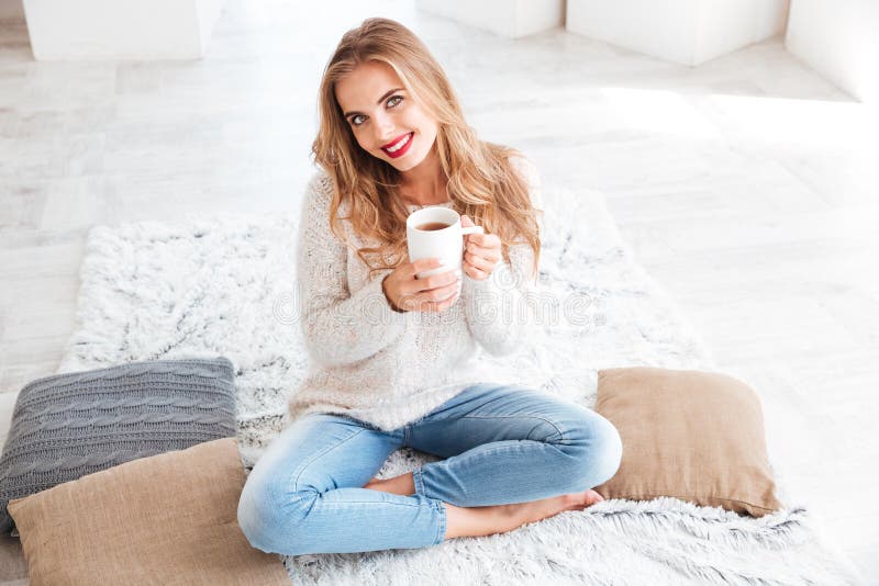 Fille heureuse tenant la tasse de thé et regardant l'appareil-photo à l'intérieur photo stock Fille heureuse tenant la tasse de thé et regardant l'appareil-photo à l'intérieur photo stock