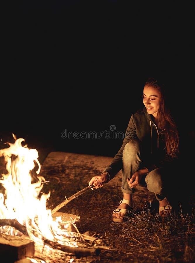 Young woman in geans and hoodie in the mountains. Young woman with fire on mountain at sunset. Girl standing near a fireplace. Young woman in geans and hoodie in the mountains. Young woman with fire on mountain at sunset. Girl standing near a fireplace