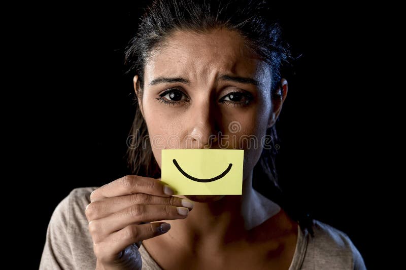 Fille latine déprimée triste latine tenant le papier cachant sa bouche derrière le sourire dessiné par faux photo stock Fille latine déprimée triste latine tenant le papier cachant sa bouche derrière le sourire dessiné par faux photo stock