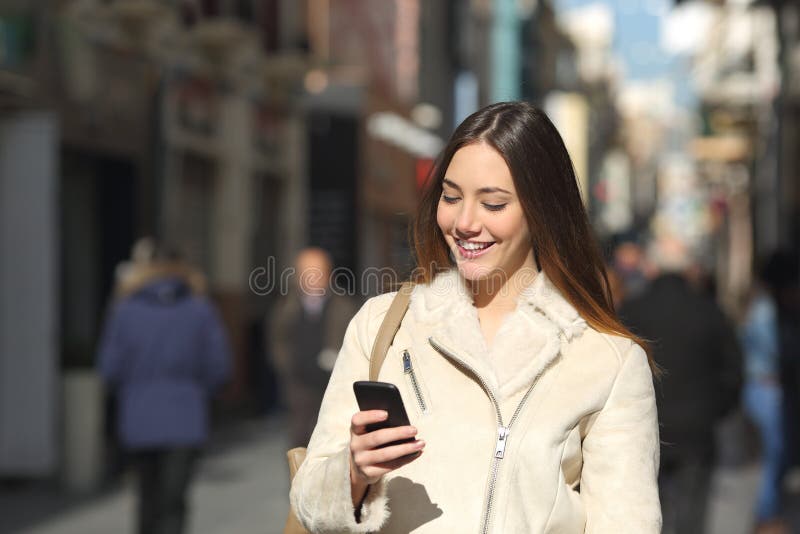 Fille marchant et textotant au téléphone intelligent dans la rue en hiver photo libre de droits Fille marchant et textotant au téléphone intelligent dans la rue en hiver photo libre de droits