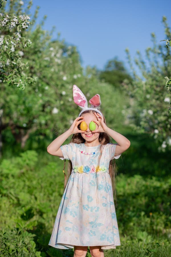Fille mignonne avec des oreilles de lapin le jour de Pâques Une fille chasse des oeufs de pâques dans le jardin photo libre de droits Fille mignonne avec des oreilles de lapin le jour de Pâques Une fille chasse des oeufs de pâques dans le jardin photo libre de droits