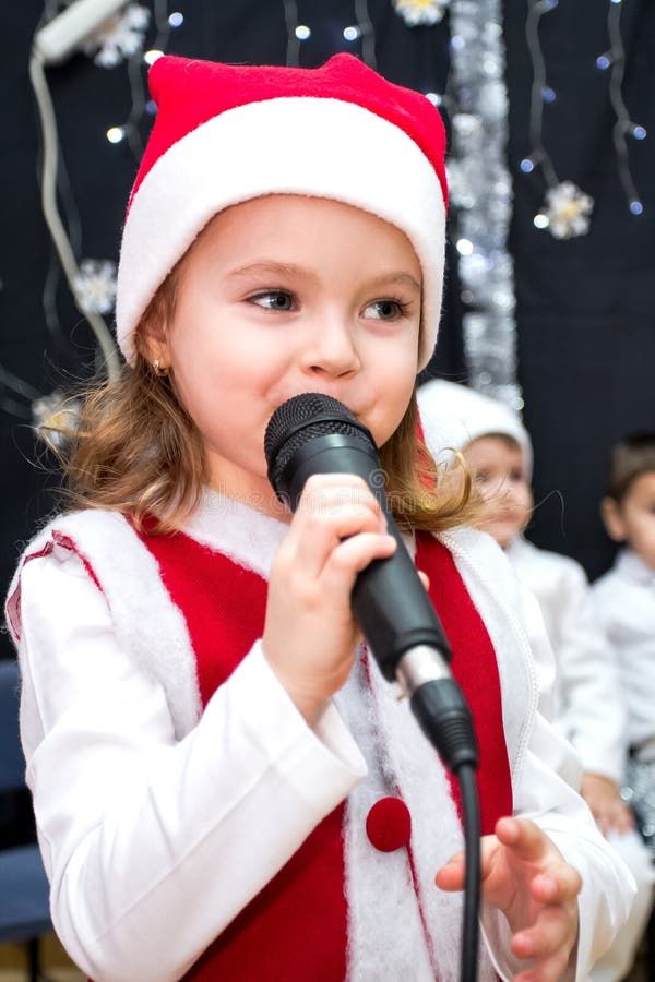 Fille mignonne dans la robe rouge de Santa tenant le microphone sur l'étape photos libres de droits Fille mignonne dans la robe rouge de Santa tenant le microphone sur l'étape photos libres de droits