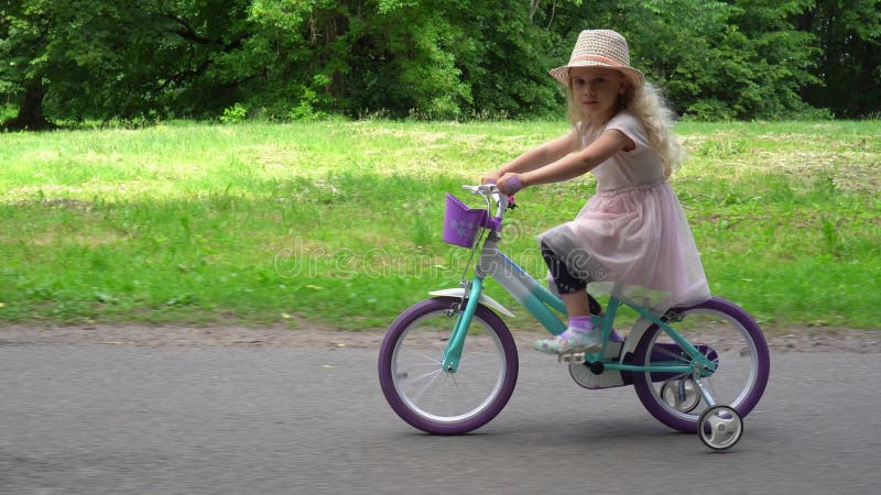 Fille mignonne de sourire faisant un cycle en parc Tir de mouvement de parallèle de cardan banque de vidéos