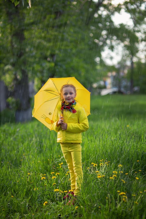 Fille mignonne drôle portant le manteau jaune tenant le parapluie coloré jouant dans le jardin par le temps de pluie et de soleil images stock Fille mignonne drôle portant le manteau jaune tenant le parapluie coloré jouant dans le jardin par le temps de pluie et de soleil images stock