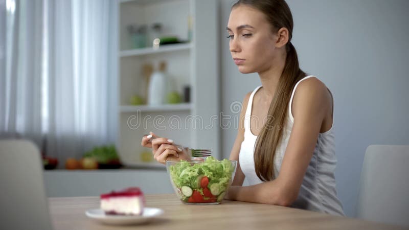 Fille mince mangeant de la salade mais implorant le gâteau, tendance de mode d'être mince, régime image libre de droits Fille mince mangeant de la salade mais implorant le gâteau, tendance de mode d'être mince, régime image libre de droits