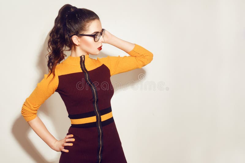 Fille modèle de brune de mode de beauté portant les lunettes élégantes Femme sexy avec le maquillage parfait, la robe orange et r photo stock Fille modèle de brune de mode de beauté portant les lunettes élégantes Femme sexy avec le maquillage parfait, la robe orange et r photo stock