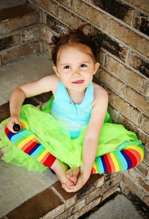 Portrait of a young girl sitting on brick steps eating a lollipop, wearing rainbow tights and a bright green tutu. Portrait of a young girl sitting on brick steps eating a lollipop, wearing rainbow tights and a bright green tutu