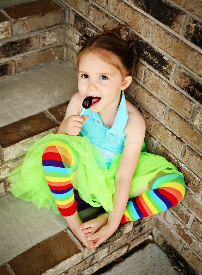 Portrait of a young girl sitting on brick steps eating a lollipop, wearing rainbow tights and a bright green tutu. Portrait of a young girl sitting on brick steps eating a lollipop, wearing rainbow tights and a bright green tutu