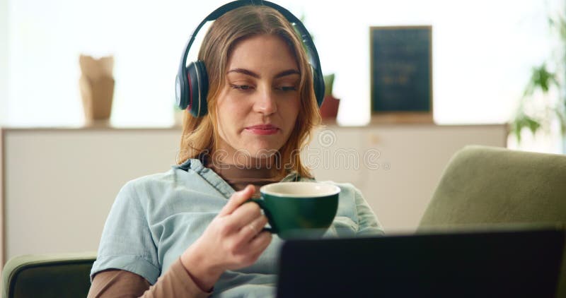 Fille relax et casque avec ordinateur portable sur canapé pour écouter musique éducation podcast et café pause. femme rire et banque de vidéos