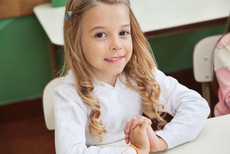 Fille s'asseyant avec des mains étreintes dans la salle de classe photo stock Fille s'asseyant avec des mains étreintes dans la salle de classe photo stock