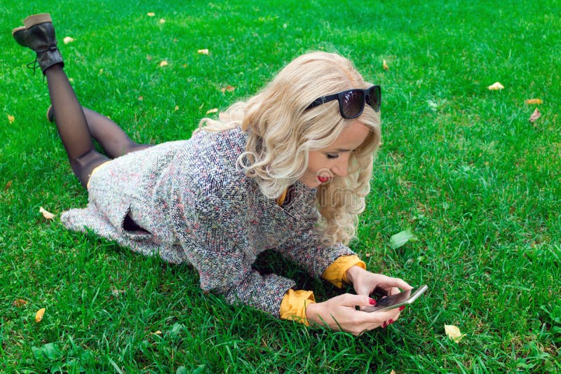 Fille se trouvant sur l'herbe et tenant un téléphone photo stock Fille se trouvant sur l'herbe et tenant un téléphone photo stock