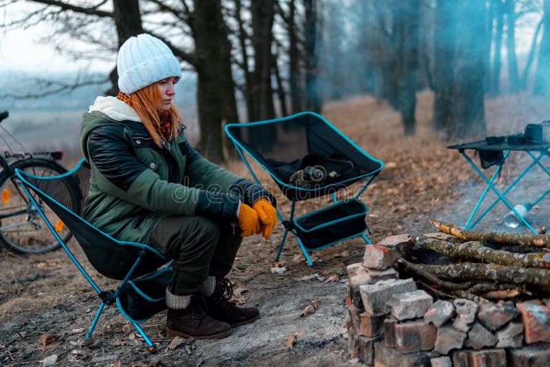 Girl sitting alone on light chairs by the fire. Cold autumn evening in the forest. The concept of an active lifestyle, travel, vacation. campfire. Girl sitting alone on light chairs by the fire. Cold autumn evening in the forest. The concept of an active lifestyle, travel, vacation. campfire