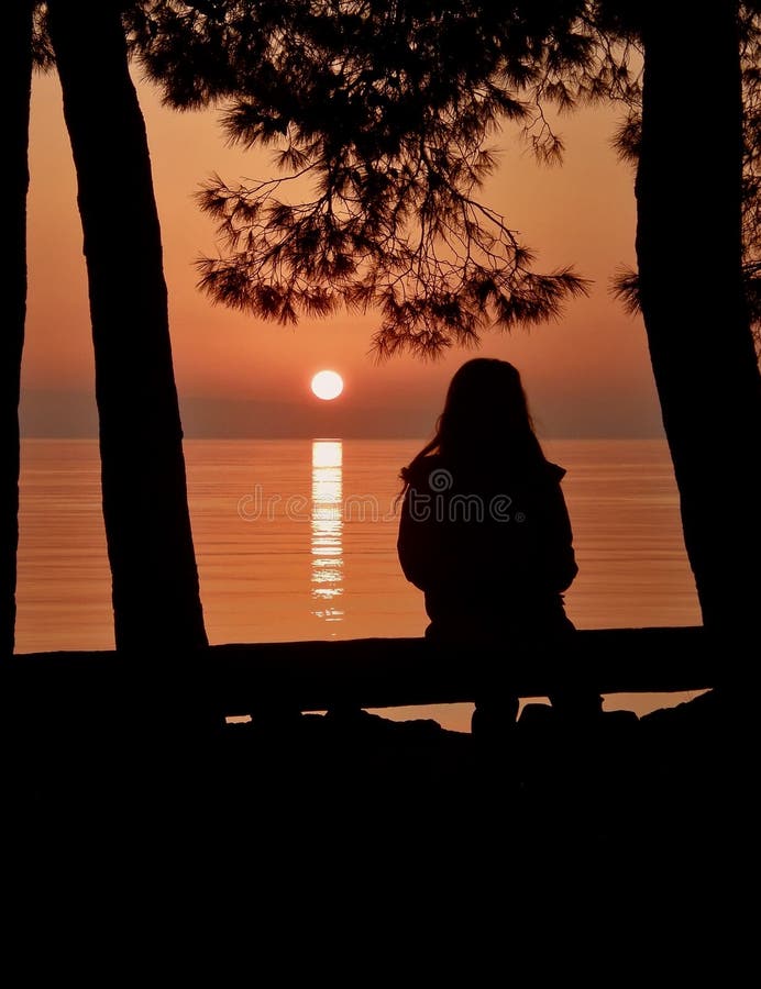 A little alone young girl sitting near the Adriatic under a pine trees and enjoying to watching the beautiful sunset at Croatia. A little alone young girl sitting near the Adriatic under a pine trees and enjoying to watching the beautiful sunset at Croatia.
