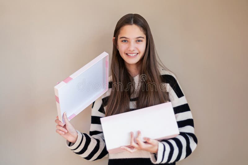 Fille souriante tenant une boîte cadeau rose ouverte. une jeune fille joyeuse aux cheveux longs bruns sourit tout en tenant un ouv image stock