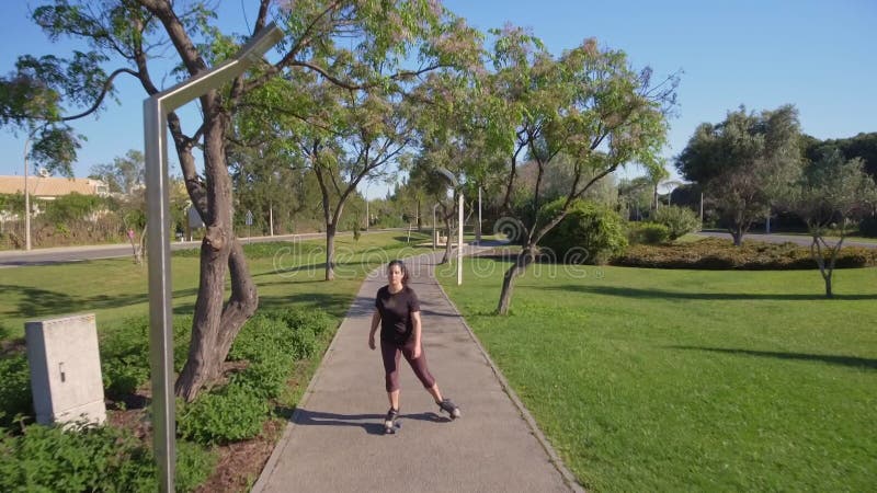 Fille sportive sur roulettes. conduite sur asphalte dans un parc verdoyant. vue frontale. banque de vidéos