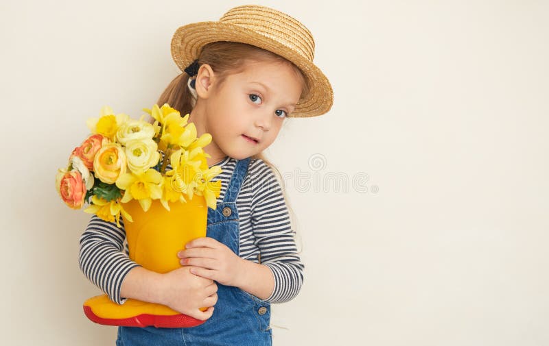 Fille surprise peu d'enfant dans le chapeau de paille avec un bouquet de fleurs jaunes dans une chaussure en caoutchouc. Petite ai photo stock