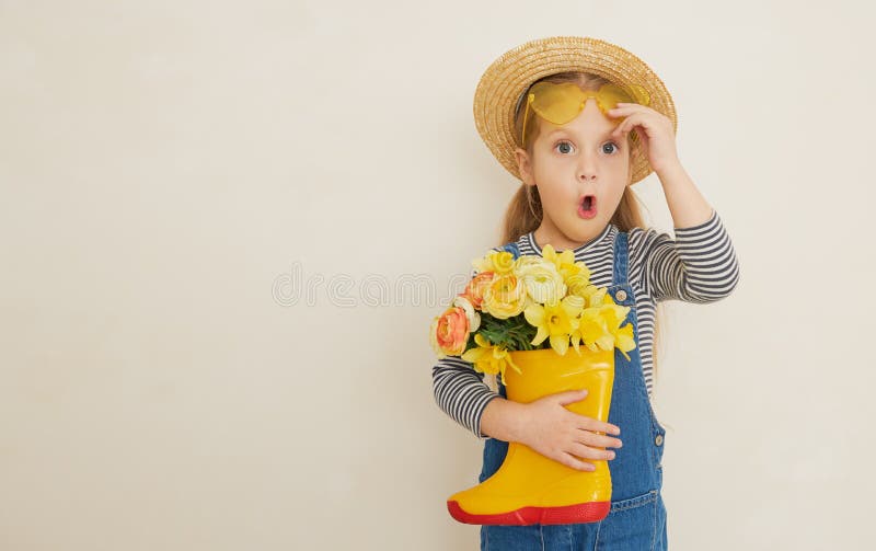 Fille surprise peu d'enfant dans le chapeau de paille avec un bouquet de fleurs jaunes dans une chaussure en caoutchouc. Petite ai photos libres de droits