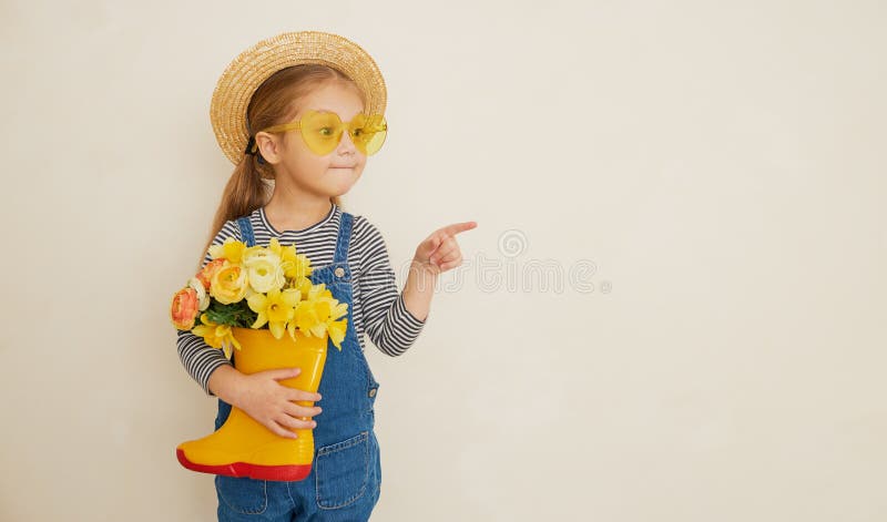 Fille surprise peu d'enfant dans le chapeau de paille avec un bouquet de fleurs jaunes dans une chaussure en caoutchouc. Petite ai photo stock