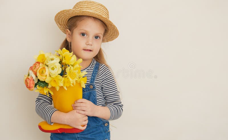 Fille surprise peu d'enfant dans le chapeau de paille avec un bouquet de fleurs jaunes dans une chaussure en caoutchouc. photographie stock