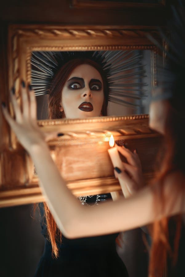 Fille étrange de goth jugeant la bougie disponible et regardant dans le miroir photo stock Fille étrange de goth jugeant la bougie disponible et regardant dans le miroir photo stock