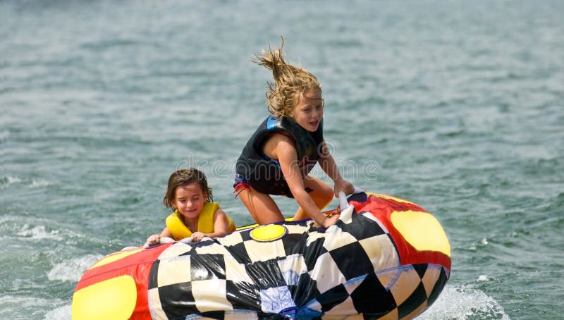 Two brave young girls on a tube being pulled behind a boat. One hanging on for dear life, the other standing and being bounced around. 6 & 7 years old. Two brave young girls on a tube being pulled behind a boat. One hanging on for dear life, the other standing and being bounced around. 6 & 7 years old.