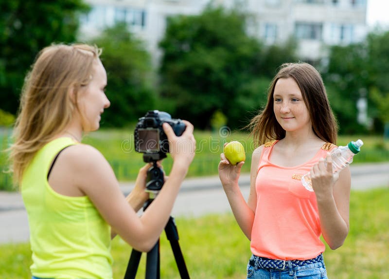 2 filles sont des adolescentes Pendant l'été en parc en nature Écrit la vidéo à l'appareil-photo Ici ` s comment tenir une pomme images libres de droits 2 filles sont des adolescentes Pendant l'été en parc en nature Écrit la vidéo à l'appareil-photo Ici ` s comment tenir une pomme images libres de droits