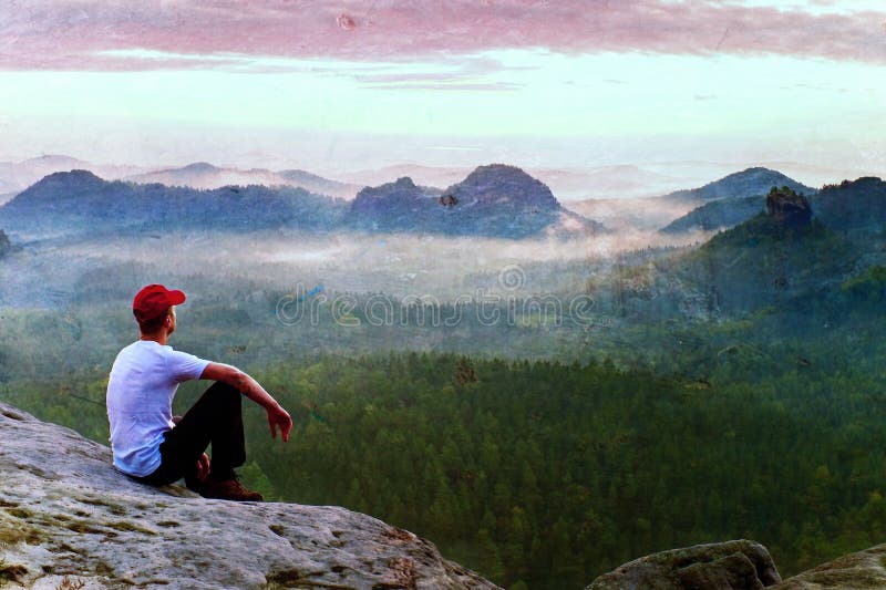 Film grain. Adult sportsman in white shirt, dark trousars and red cap. Man sit on sharp cliff