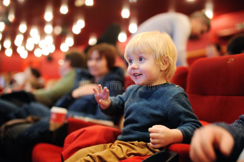 Filme de observação dos desenhos animados do menino bonito da criança no cinema foto de stock Filme de observação dos desenhos animados do menino bonito da criança no cinema foto de stock