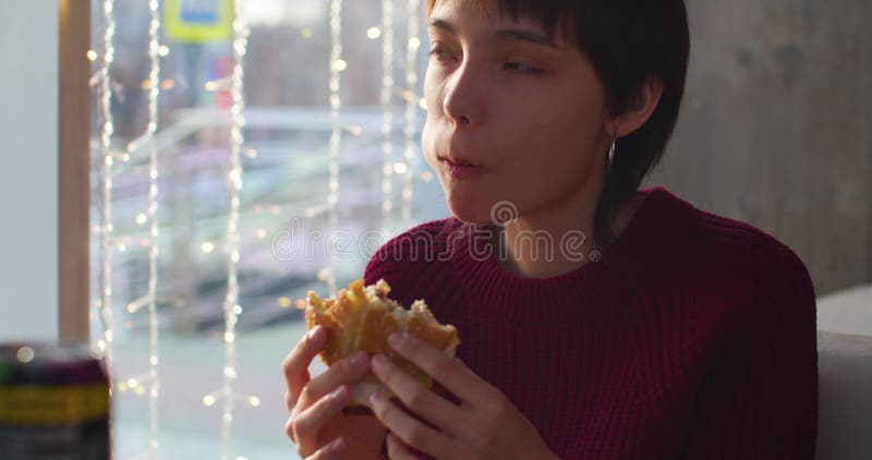 Filmer une adolescente mangeant du burger assis dans un café. banque de vidéos
