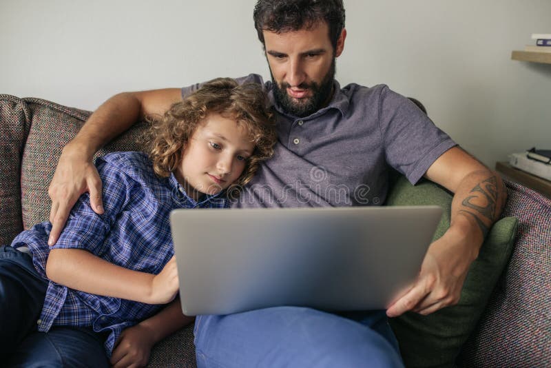 Filmes de observação do pai e do filho novo em um portátil imagens de stock Filmes de observação do pai e do filho novo em um portátil imagens de stock