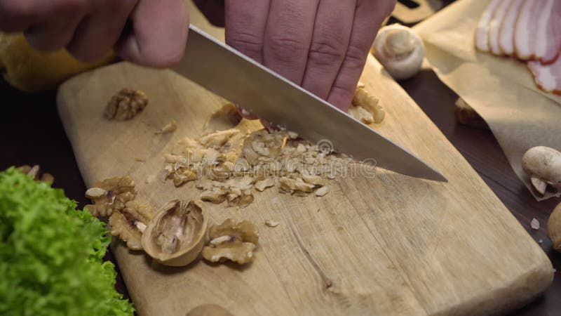 Fim acima do vídeo: nozes dos cortes do cozinheiro chefe na placa de madeira, cozinhando a salada, alimento do vegetariano da vit