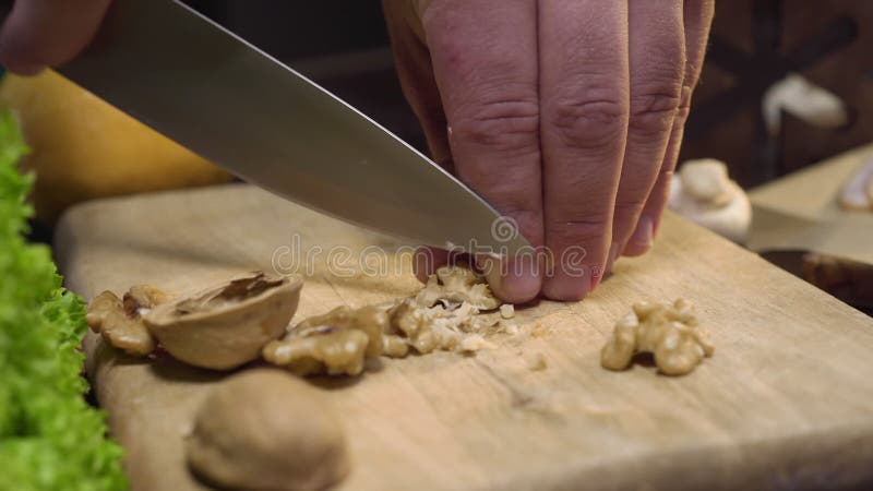 Fim acima do vídeo: nozes dos cortes do cozinheiro chefe na placa de madeira, cozinhando a salada, alimento do vegetariano da vit