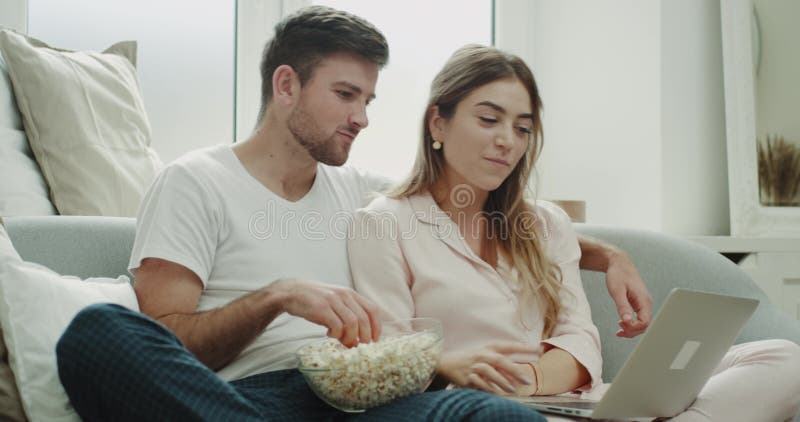 Fin de semana carismático del gasto de los pares juntas que come las palomitas y que mira algo en el ordenador portátil