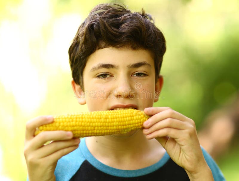 Fine bollita mangiare della pannocchia di granturco del ragazzo dell'adolescente sulla foto fotografie stock Fine bollita mangiare della pannocchia di granturco del ragazzo dell'adolescente sulla foto fotografie stock