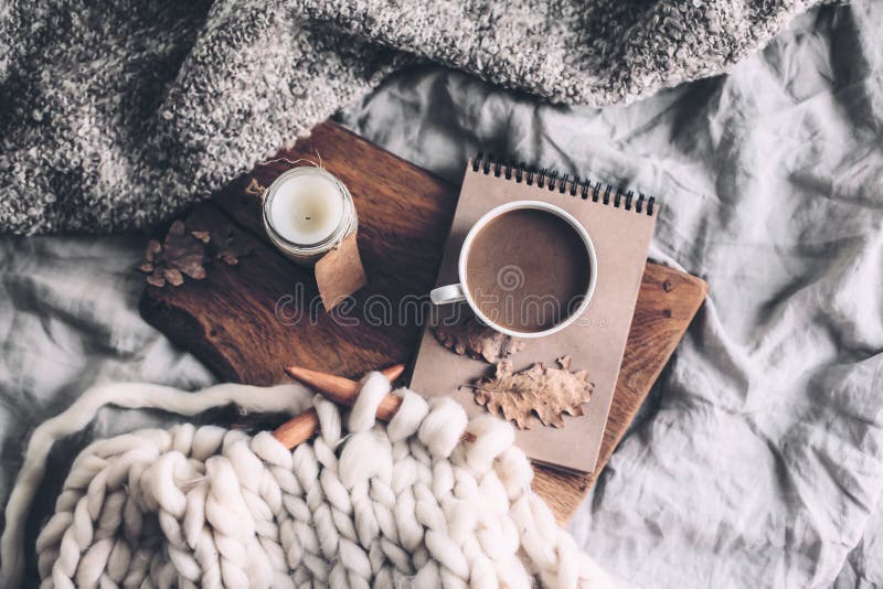 Cup of coffee and candle on rustic wooden serving tray in the cozy bed with blanket. Knitting warm woolen sweater in the autumn weekend, top view. Cup of coffee and candle on rustic wooden serving tray in the cozy bed with blanket. Knitting warm woolen sweater in the autumn weekend, top view.