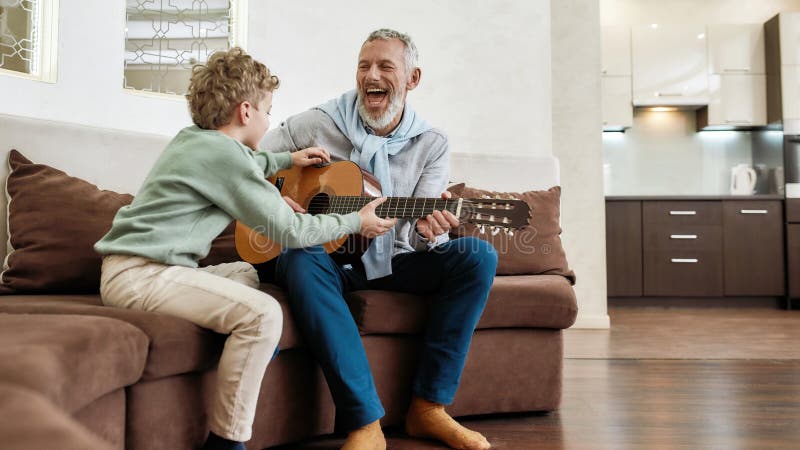 Fine settimana con il nonno. uomo maturo e allegro nonno che suona la chitarra al suo piccolo nipote carino fotografia stock