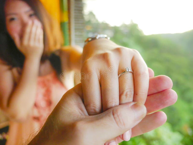 Fine sull'uomo delle mani delle coppie che tiene la mano felice del fidanzato con l'anello di fidanzamento del diamante sul suo d