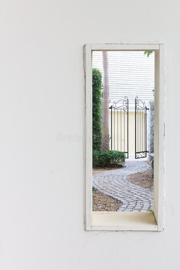 Finestra bianca della parete con il passaggio pedonale nella vista del giardino fotografia stock libera da diritti Finestra bianca della parete con il passaggio pedonale nella vista del giardino fotografia stock libera da diritti